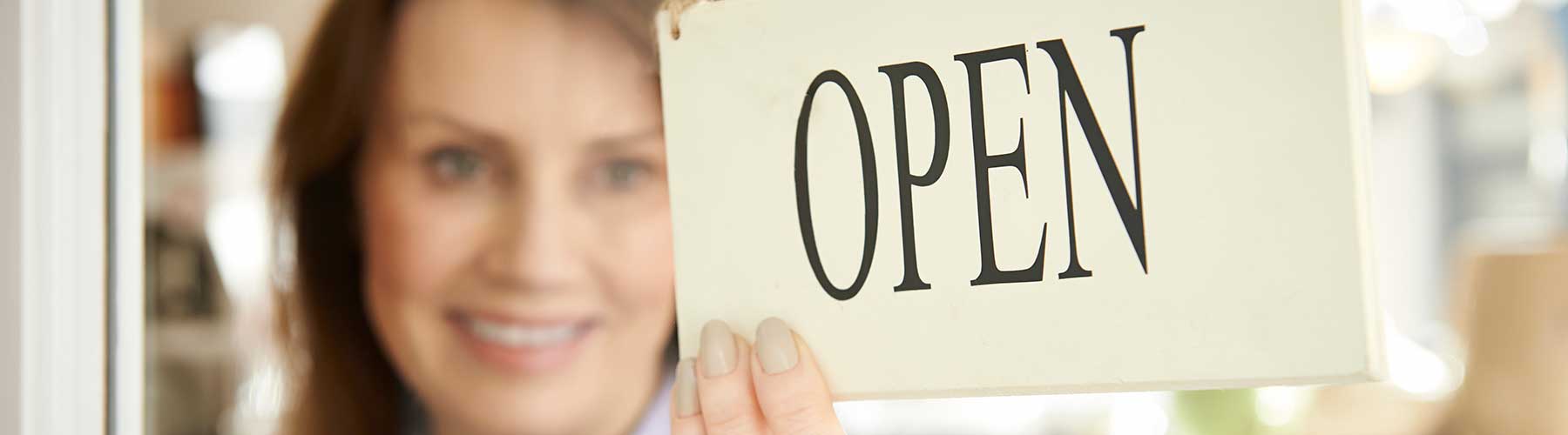 Business insurance represented by a woman placing an open sign in a shop window